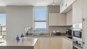A modern kitchen with a large island, built-in appliances, and a view of the sea.
