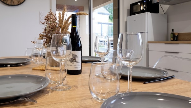 A dining table set with plates, wine glasses, and a bottle of French Boulèdogue wine. - Cottage Brocéliande * SPA * Terrace * Location * (La Gacilly)