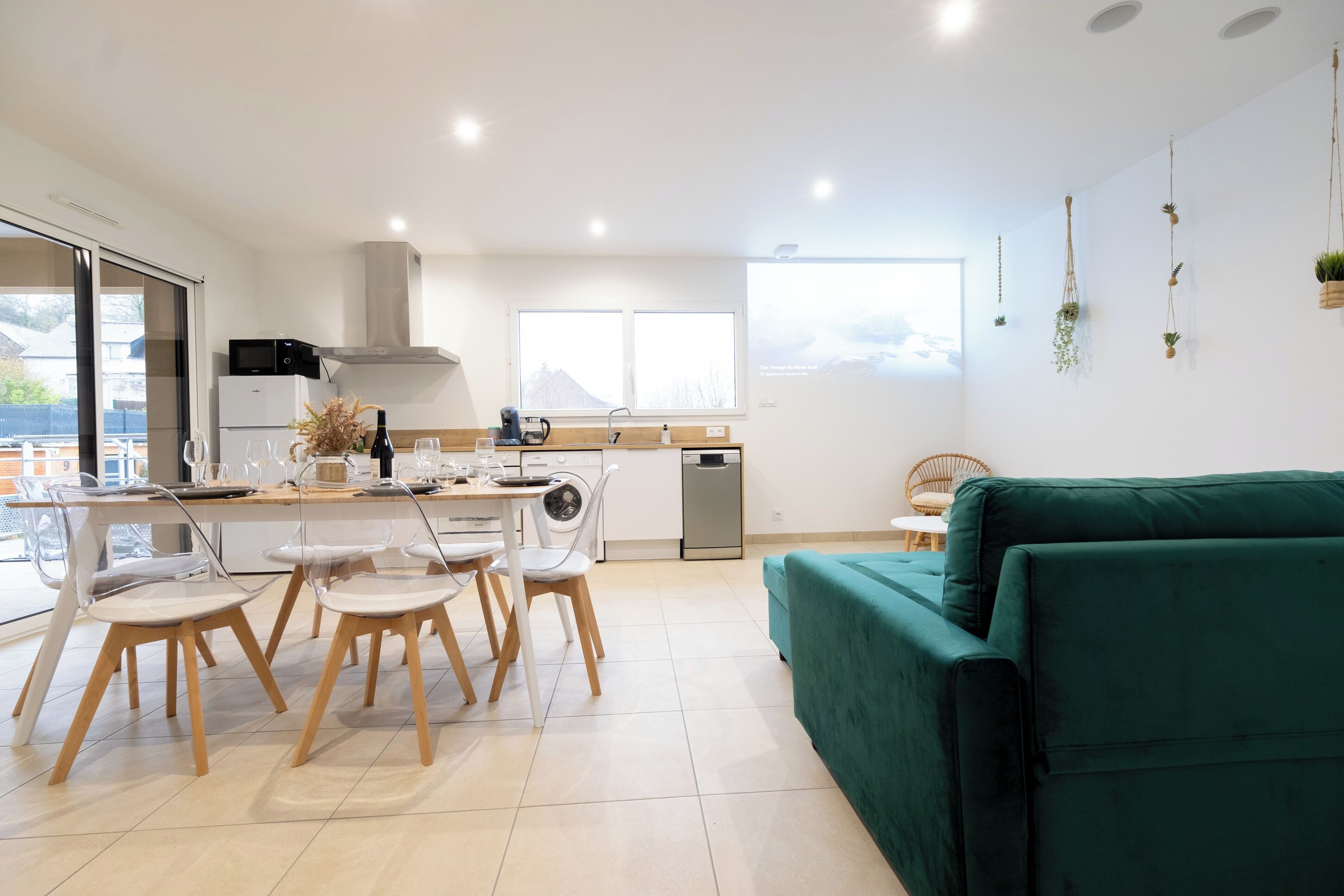 A modern kitchen with a dining area, a green sofa, and a view of mountains through the windows.