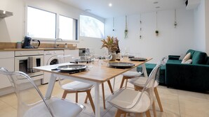 A modern kitchen with a dining area, including a wooden table, clear chairs, and a green sofa. - Cottage Brocéliande * SPA * Terrace * Location * (La Gacilly)