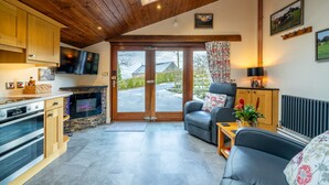 A modern kitchen with built-in appliances, a stone fireplace, and a large sliding glass door leading to a patio. - Stoney Calf -  Quaint Cottage for two on a working farm (Old Town)