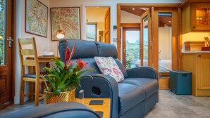 A modern living room with a blue sofa, wooden chair, and a small table with a lamp and plant. - Stoney Calf -  Quaint Cottage for two on a working farm (Old Town)