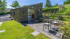 A stone building with a door and windows, a paved patio with chairs, and a wooden fence. - Stoney Calf -  Quaint Cottage for two on a working farm (Old Town)