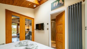 A bedroom with a bed, a TV, a shower, and a wooden door. - Stoney Calf -  Quaint Cottage for two on a working farm (Old Town)