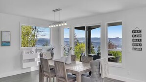A dining area with a view of mountains and a lake, a white wall with a sign, and a modern chandelier.