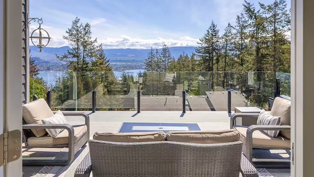 A balcony with wicker furniture, a glass railing, and a view of a lake and mountains.