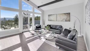 A modern living room with a large glass door leading to an outdoor area, a grey sofa, a coffee table, and abstract wall art.
