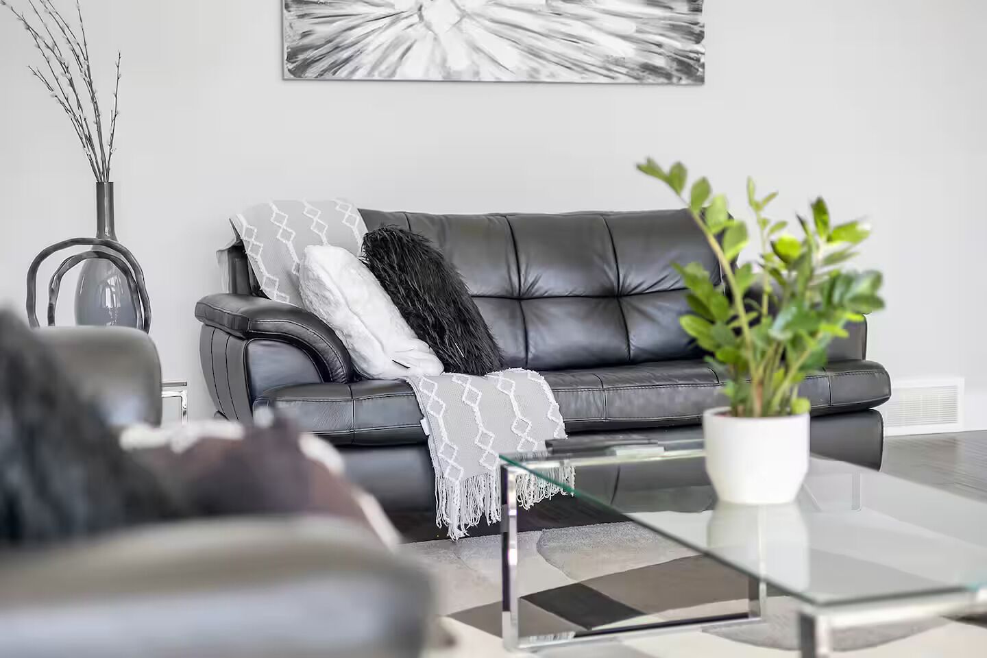 Una sala de estar moderna con un sofá de cuero negro, una mesa de centro de vidrio y una planta en maceta.