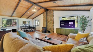 A spacious living room with a stone fireplace, wooden ceiling beams, and a television displaying a welcome message.