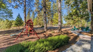 A playground with a red swing set and a slide, surrounded by trees and a paved path.