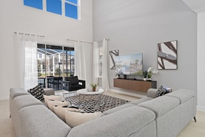 Uma sala de estar moderna com um sofá cinza, uma mesa de centro e uma TV sobre um suporte de madeira.