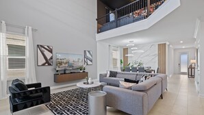 A spacious living area with a grey sofa, black armchair, and a coffee table. A staircase leads to an upper level with a balcony.