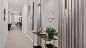 A modern hallway with a glass console table, a potted plant, and a framed artwork.