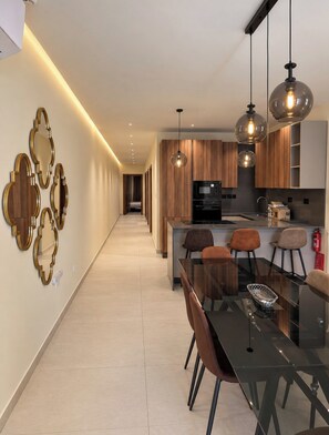 A modern kitchen with a central island, pendant lighting, and a dining area with a glass table and chairs. - Gżira 3-Bedroom Promenade Apartment Near Valletta by Malta Weekend (Il-Gzira)