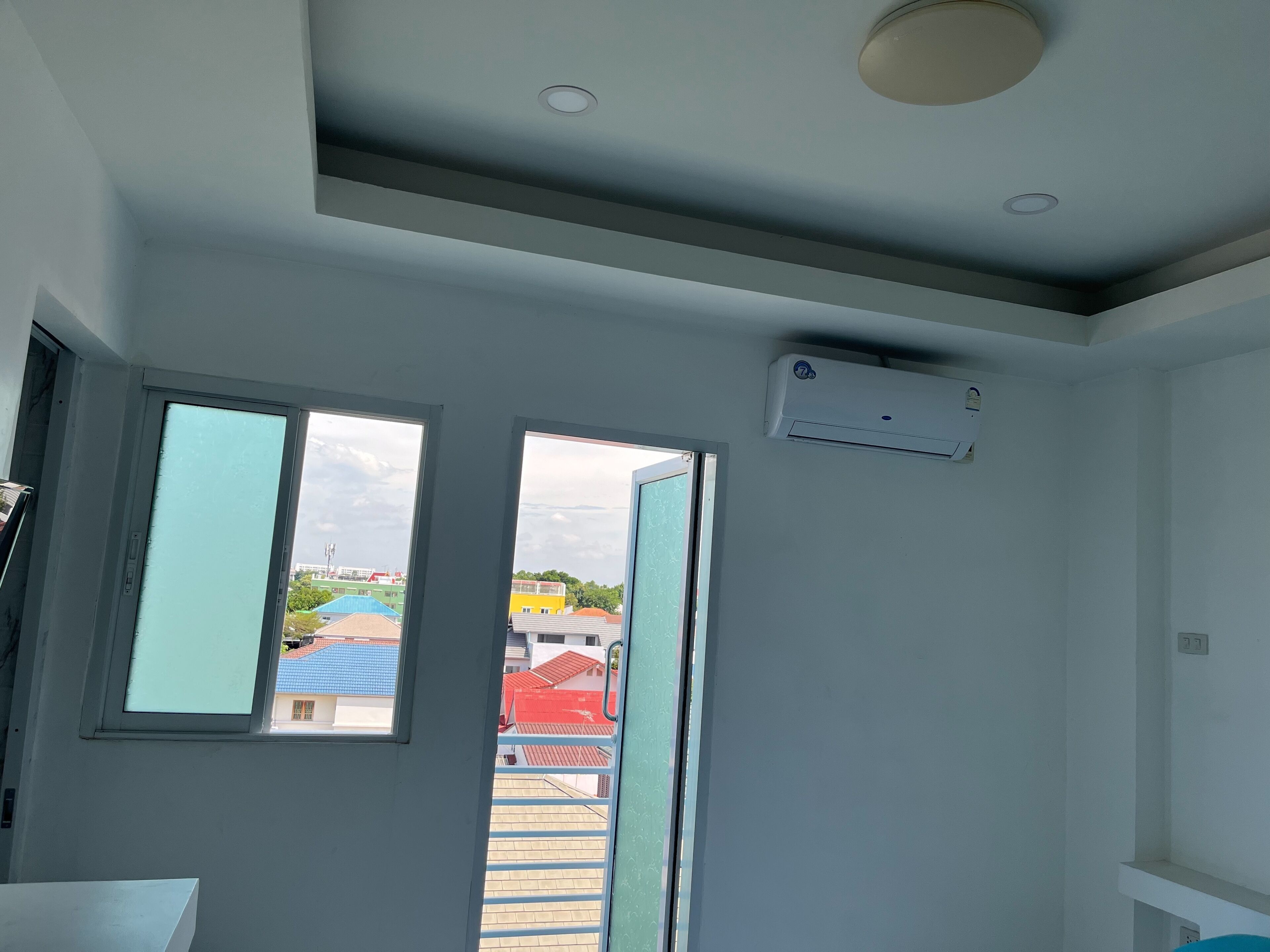 Une pièce dotée d’une grande fenêtre, d’un climatiseur et d’un luminaire au plafond.