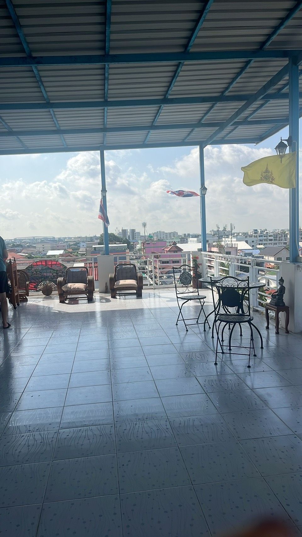 A covered outdoor area with tiled flooring, several chairs, a table, and a flag.