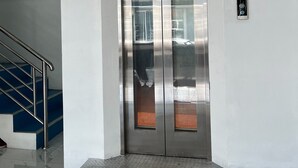 A modern elevator with metallic doors and a handrail, leading to a staircase with blue steps. - Alisara Apartments (Bangkok)