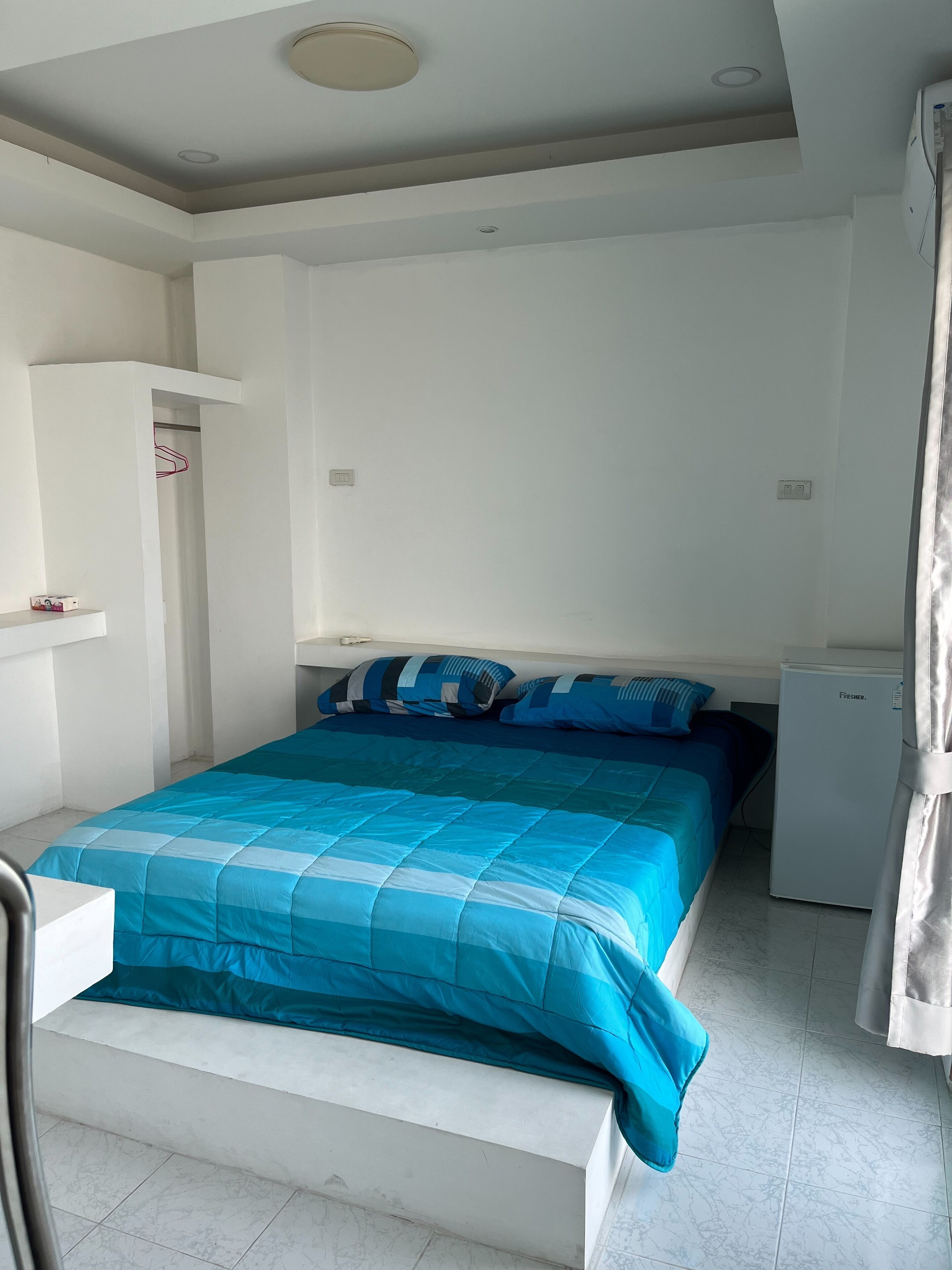 Ein Schlafzimmer mit einem Bett, einem kleinen Kühlschrank und einem weißen Kleiderschrank.