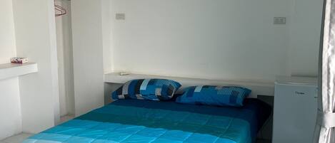 Ein Schlafzimmer mit einem Bett, einem kleinen Kühlschrank und einem weißen Kleiderschrank.