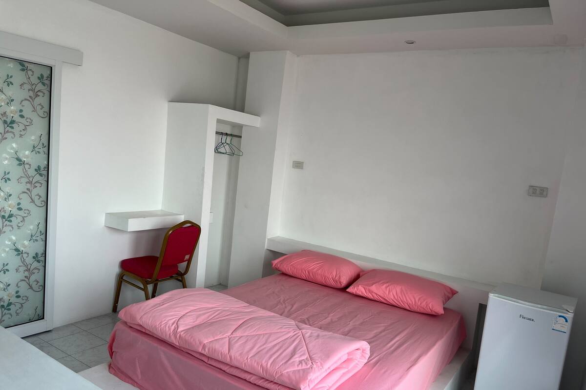 A bedroom with a bed, a desk, a chair, and a small refrigerator.