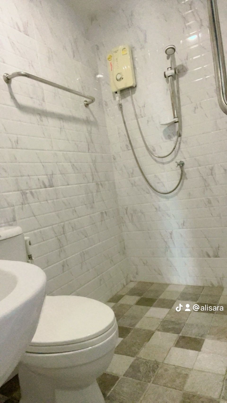 A bathroom with a toilet, a shower with a handheld showerhead, and a wall-mounted control panel.