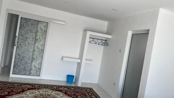 Une pièce avec un tapis à motifs, une porte coulissante ornée de rideaux à fleurs, une poubelle bleue et un porte-manteau.