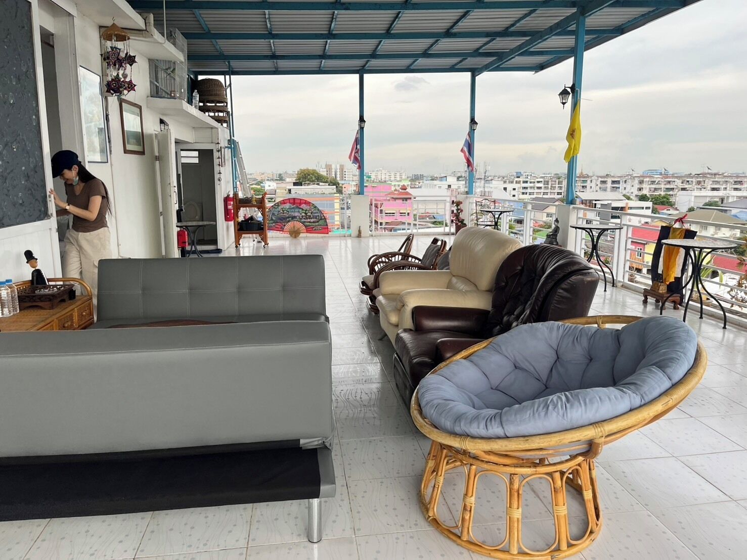 A balcony with a grey sofa, a wicker chair, and a table with a bottle and a figurine.