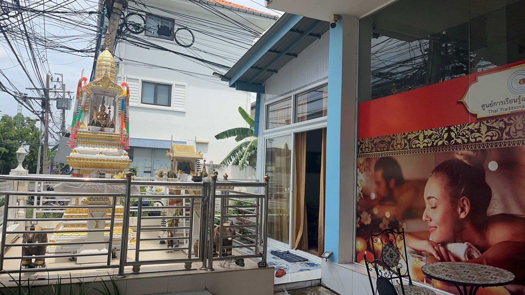 A traditional Thai temple with a golden statue, a white building with a blue door, and a poster advertising Thai traditional massage.
