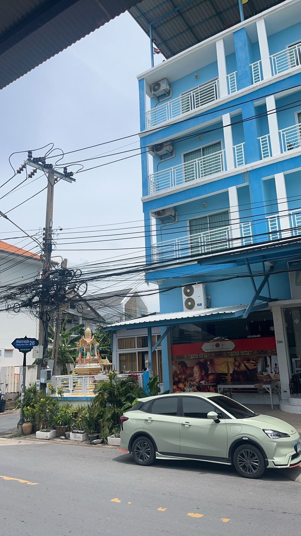 A multi-story building with balconies, a statue in front, and a parked car.