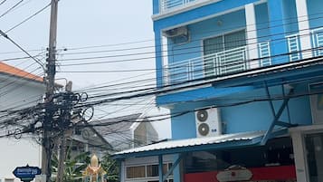 Um edifício com várias andares, varandas, uma estátua na frente e um carro estacionado.
