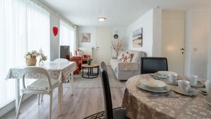 A well-lit, spacious living area with a dining table set for four, a sofa, and a small round table with a vase of flowers. - Zeelucht with private garden by Interhome (De Haan)