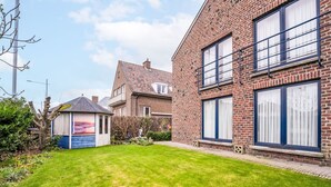 A residential area with a well-maintained lawn, a brick house with large windows, and a small shed. - Zeelucht with private garden by Interhome (De Haan)