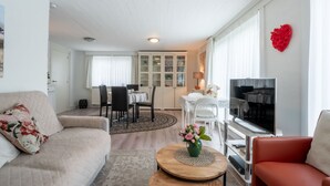 A living room with a sofa, a coffee table, a TV, and a dining area with chairs and a table. - Zeelucht with private garden by Interhome (De Haan)