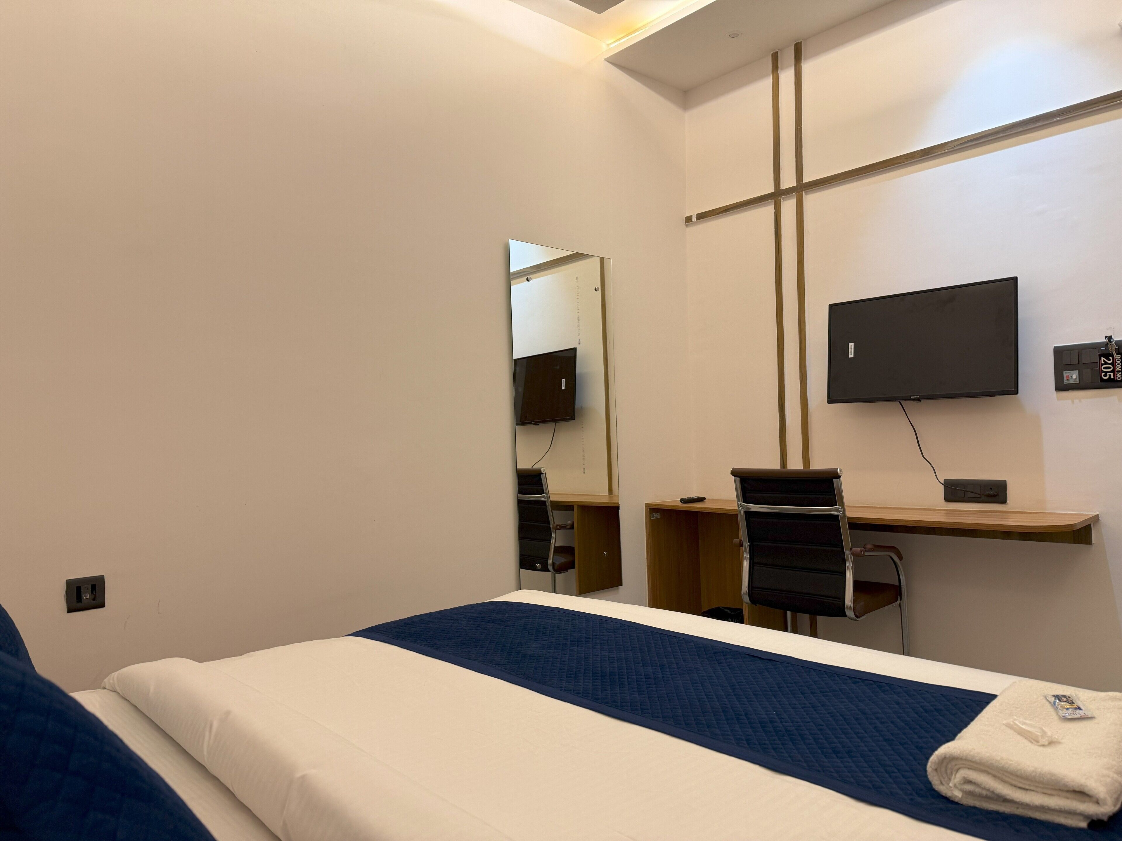A hotel room with a bed, a desk, a chair, a television, and a mirror.