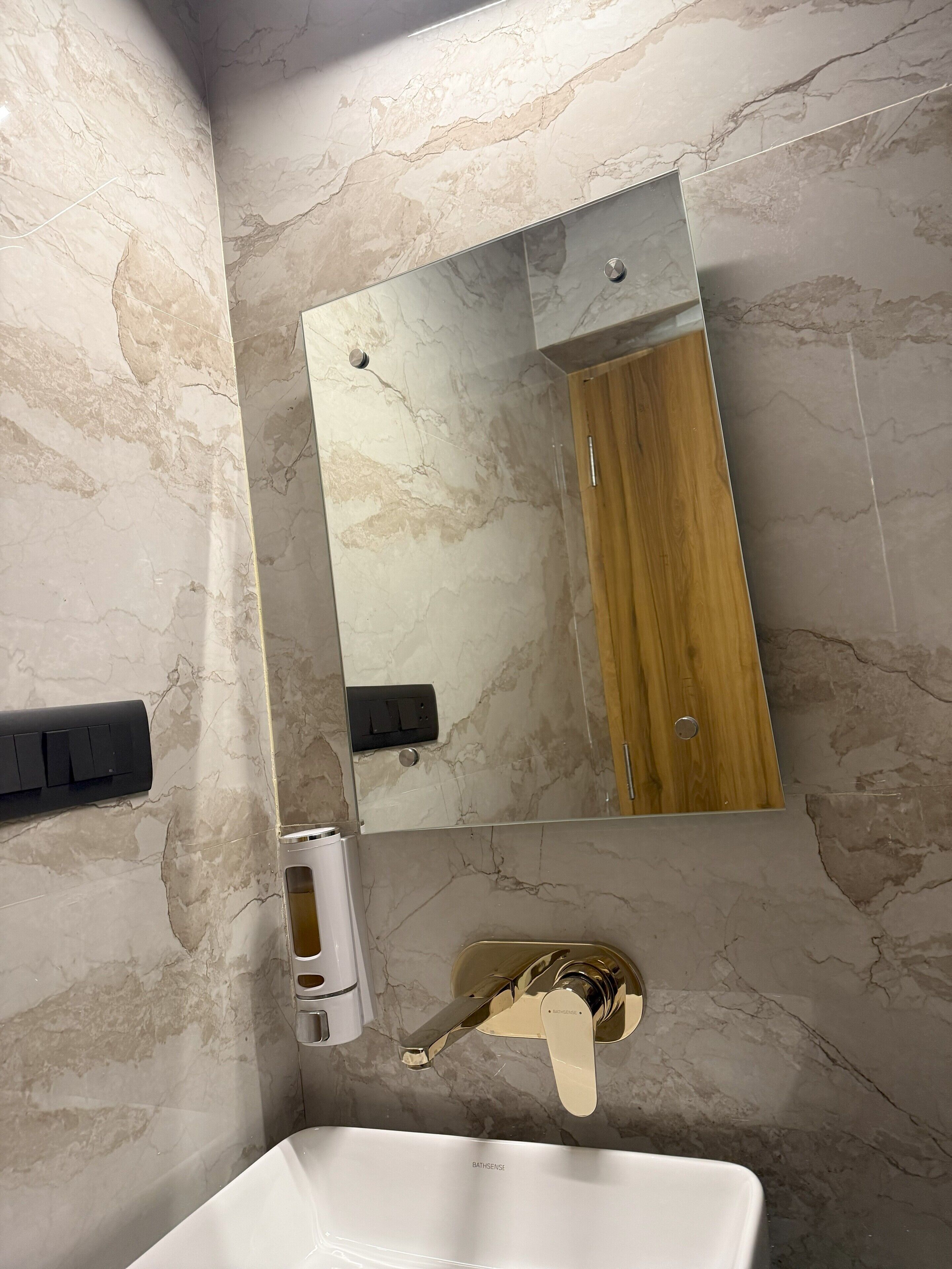 A bathroom with a marble wall, a wooden door, a white sink, and a mirror.