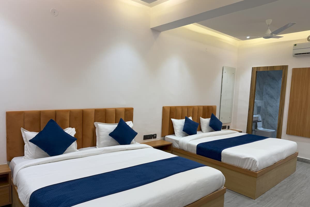 Une chambre d’hôtel avec deux lits, chacun doté d’une tête de lit en bois, de draps blancs et d’éléments décoratifs bleus. On y trouve une table de chevet entre les lits, un ventilateur de plafond et un miroir au mur.