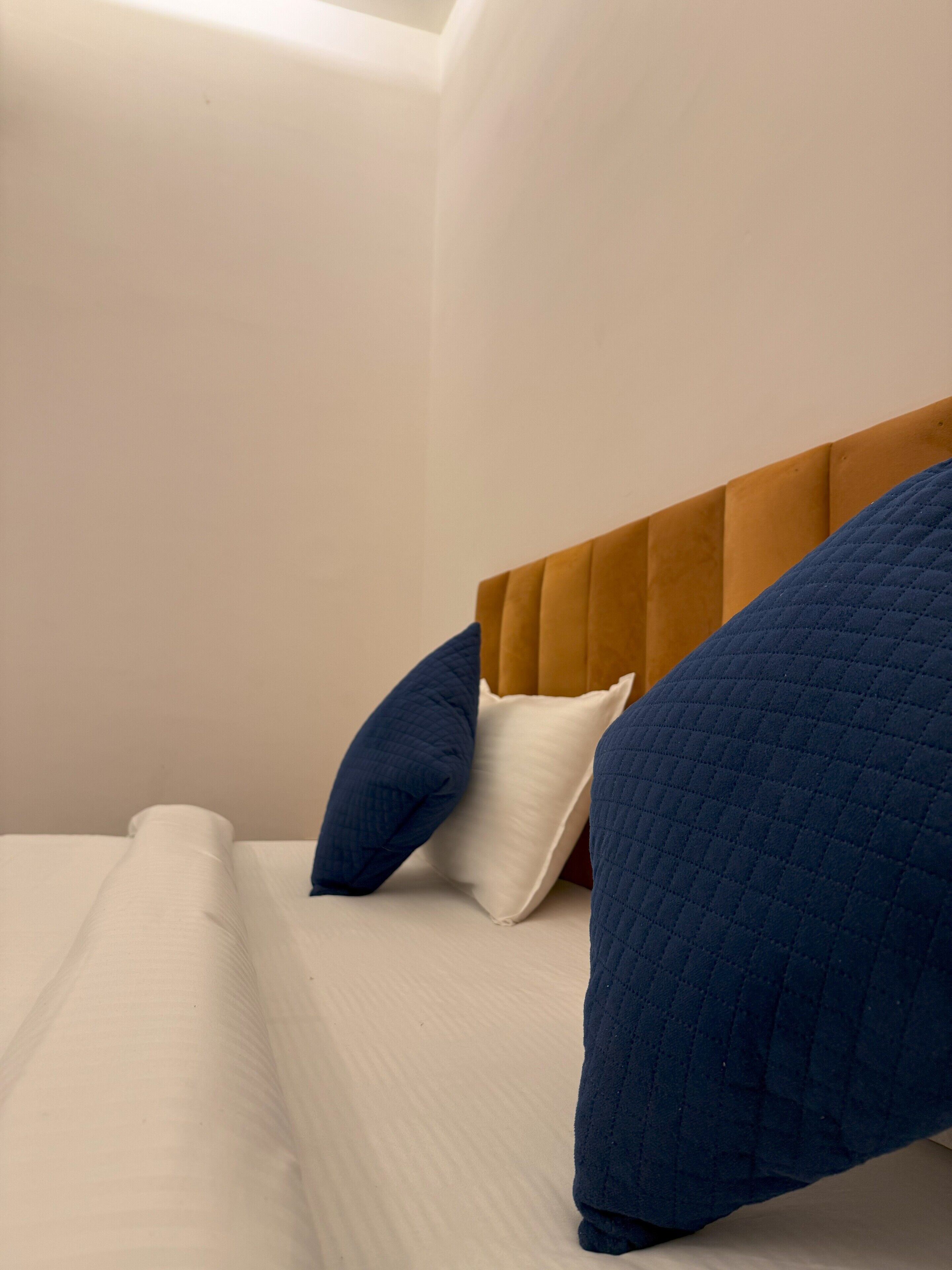 A bed with a wooden headboard, white bedding, and two blue pillows.