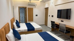 Ein Hotelzimmer mit zwei Betten, einem Schreibtisch, einem Sessel, einem Fernseher und einer Klimaanlage.