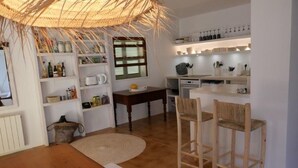 A kitchen with white shelves, a dining table with chairs, and a woven ceiling light fixture. - Son Floriany - House with private pool and lounge (Son Severa)