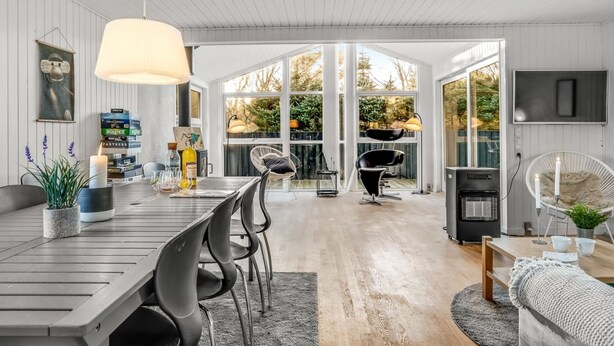Une cuisine moderne dotée d’un grand îlot central, d’un coin repas avec une table et des chaises en bois, et offrant une vue sur un jardin grâce à de grandes fenêtres.