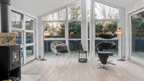 Un salon moderne avec un poêle à bois, de grandes fenêtres et deux fauteuils.