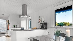 Une cuisine moderne dotée d’un îlot central, d’une machine à café et offrant une vue sur la verdure environnante.