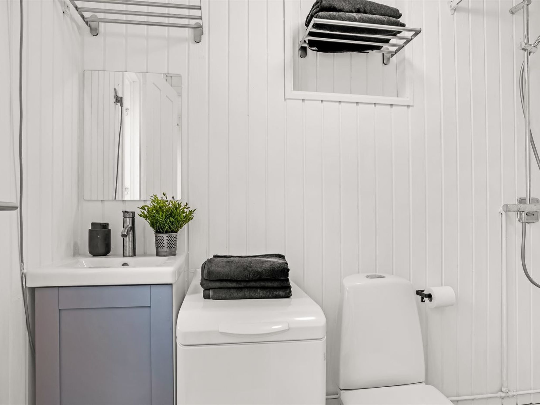 Un baño moderno con tocador blanco, inodoro, ducha y perchero para toallas.
