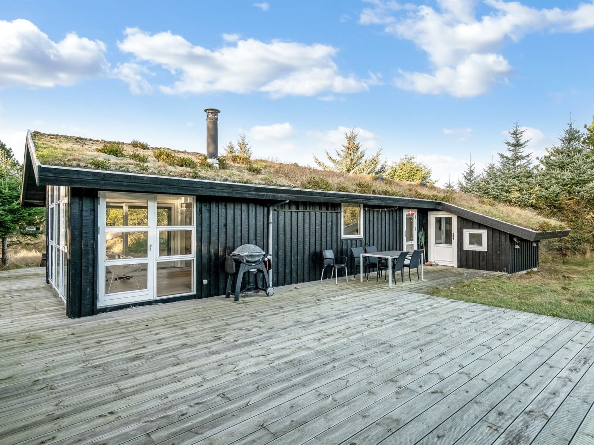 Une cabane moderne dotée d’une grande terrasse, d’un barbecue et d’une cheminée.