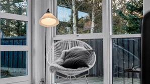 Une chambre moderne avec de grandes fenêtres, un fauteuil en osier blanc agrémenté de coussins et un lampadaire.