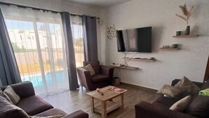 A living room with two sofas, a coffee table, a TV mounted on the wall, and a sliding glass door leading to a balcony. - Lux Villa in Island of Mauritius, Grand Baie hidden Gem with poolside Bliss (Grand Baie)