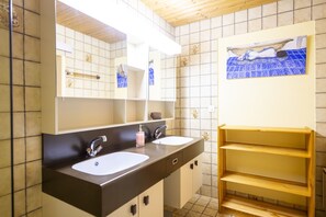 A bathroom with two sinks, a mirror, and a shelf with towels.