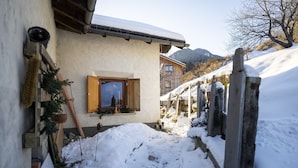 Un sentiero innevato che conduce a un edificio rustico con una finestra e un recinto in legno.