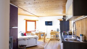 Una camera compatta con divano, tavolo da pranzo, TV e angolo cottura.
