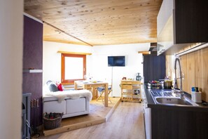 Habitación pequeña con sofá, mesa de comedor, televisor y kitchenette.